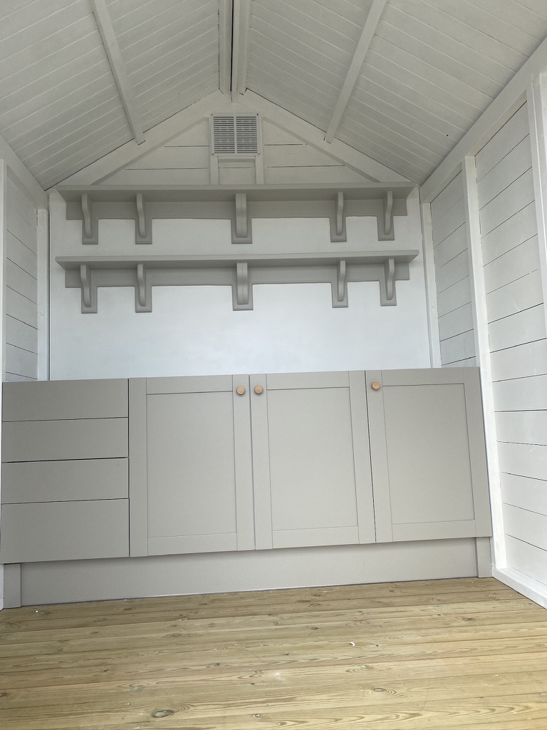 Painted summerhouse interior with fitted base cupboards, drawers and two shaped peg rail shelves