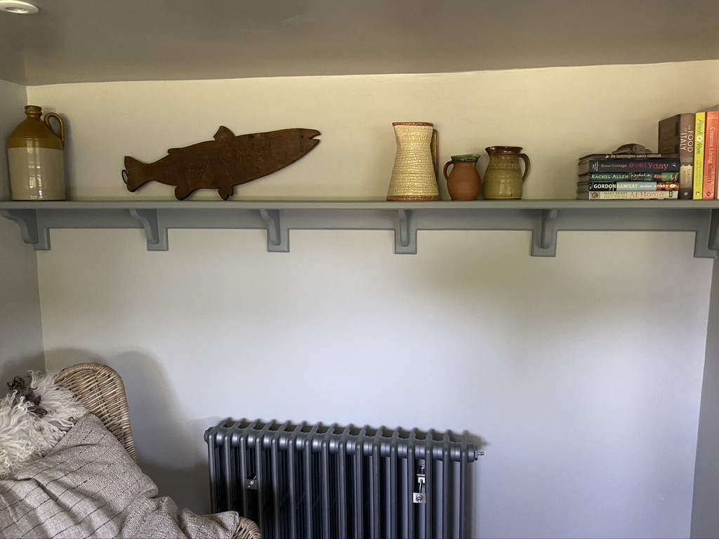 Long painted wall shelf with hand-shaped brackets, styled with pottery and books