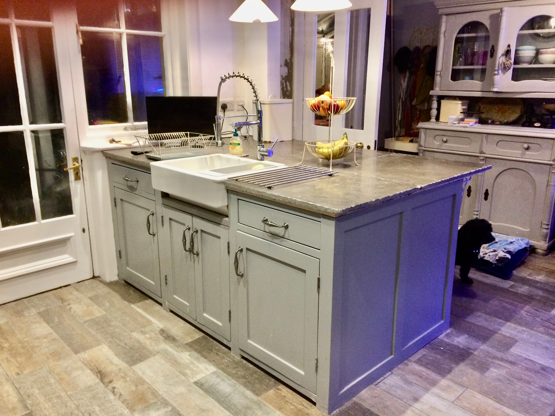 Grey painted kitchen island with Belfast sink, panelled sides and a stone worktop
