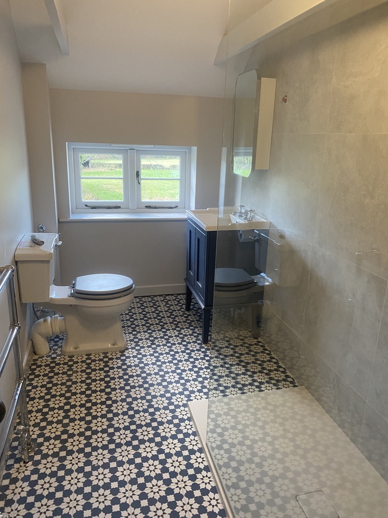 Fitted bathroom with navy vanity unit, patterned floor tiles and a walk-in tiled shower