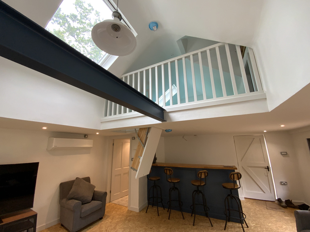 Garden room with a navy panelled bar and oak top beneath a white mezzanine balustrade