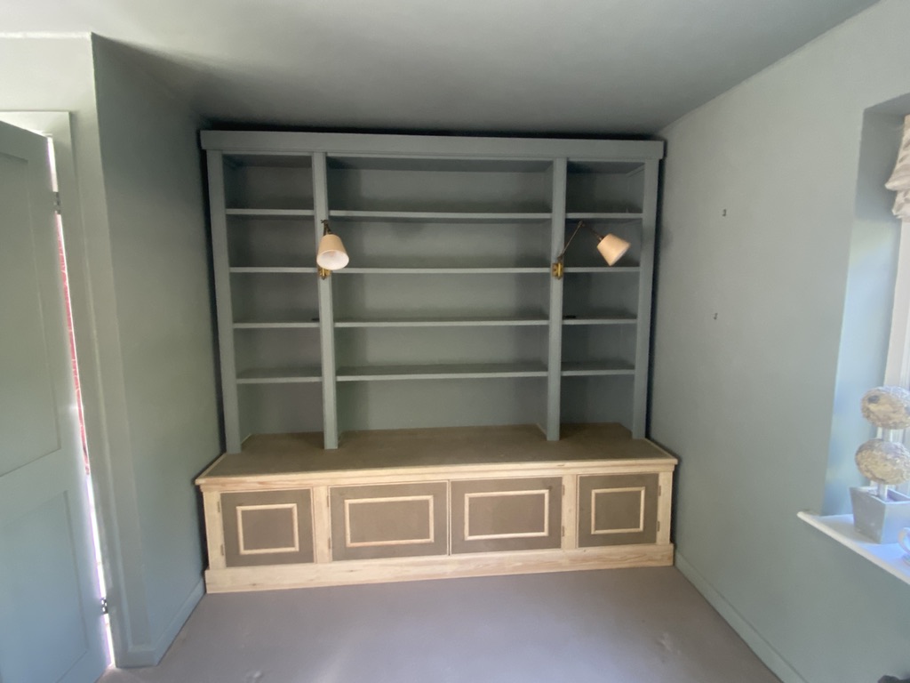 Built-in alcove shelving unit painted grey-green above a panelled bench seat with cupboards
