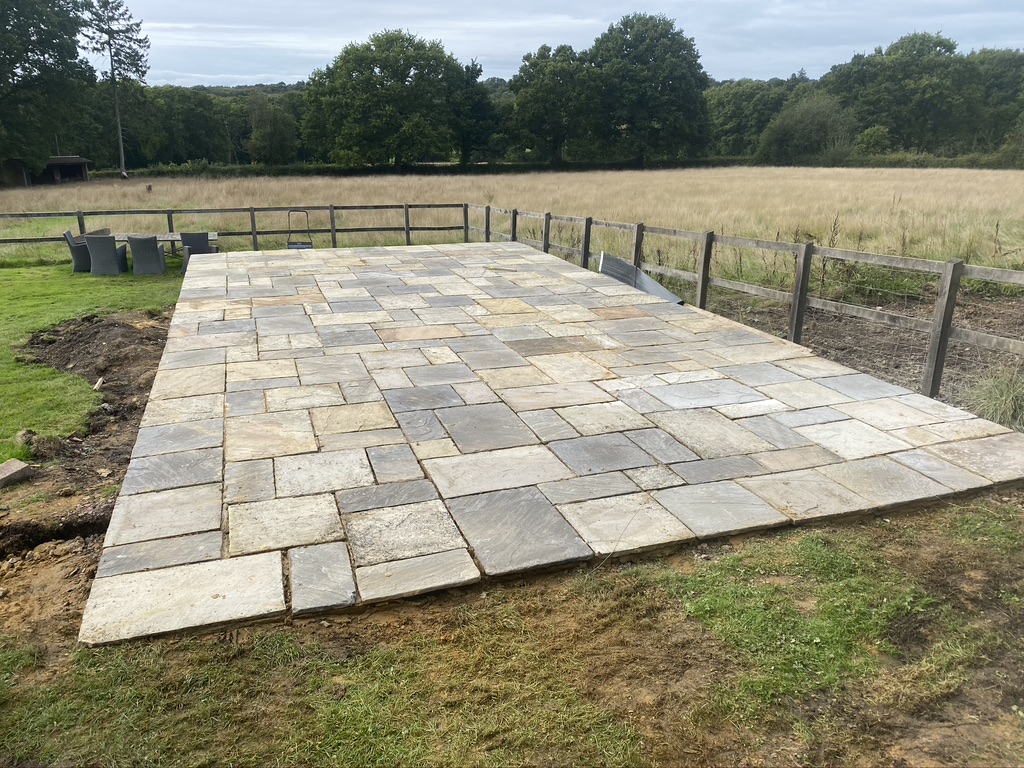 Newly laid natural stone patio in a countryside garden beside a post and rail fence