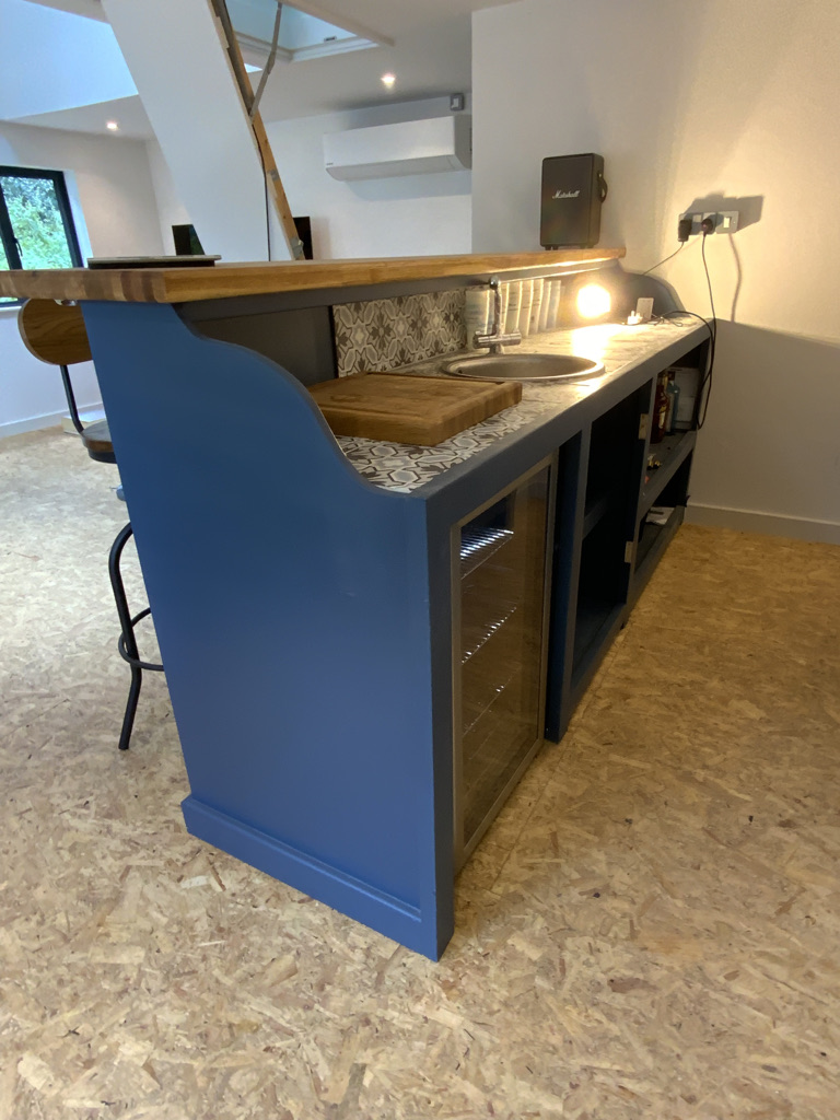 Bespoke home bar in deep blue with a solid oak top, patterned tiled splashback, sink and glazed drinks cabinet