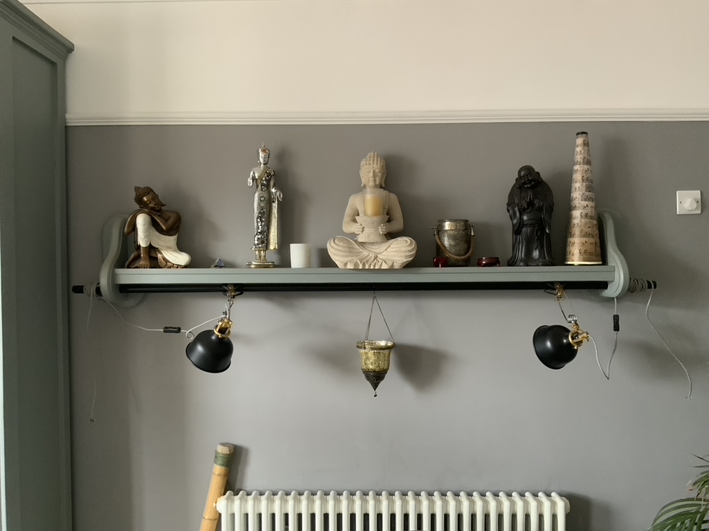 Painted wall display shelf with shaped brackets and integrated hanging lights