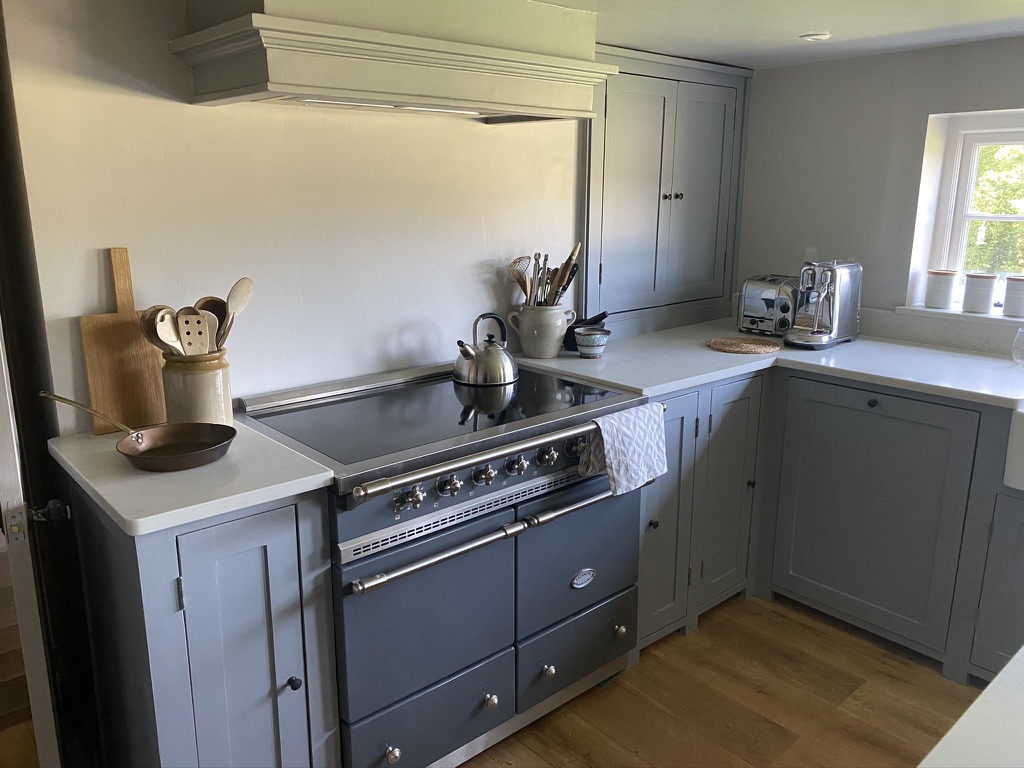 Bespoke blue-grey kitchen with a range cooker beneath a handmade extractor canopy