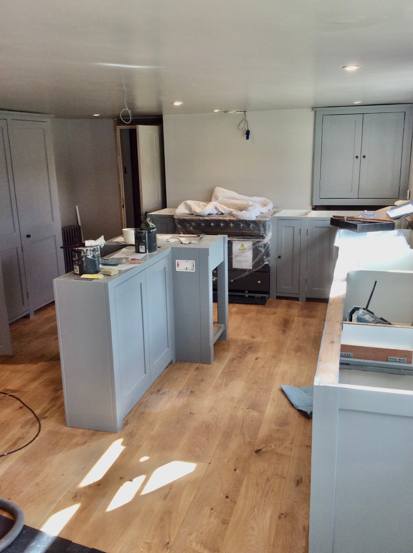 Bespoke painted kitchen mid-installation, with island, tall cupboards and oak flooring