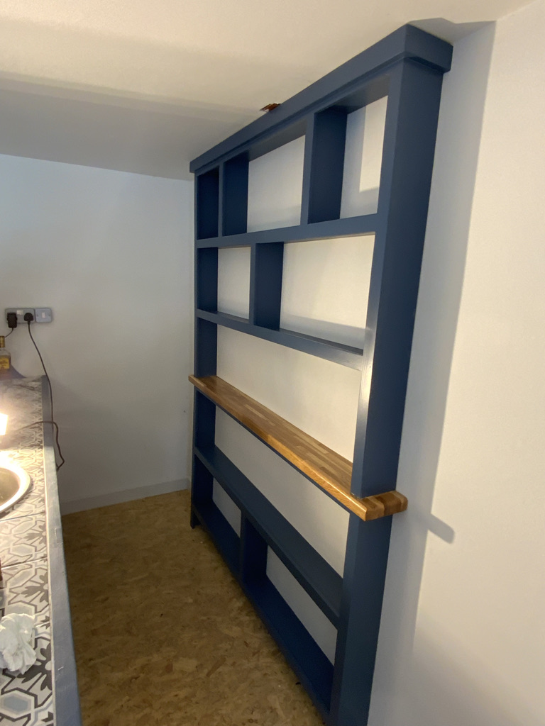 Tall navy blue open shelving unit with a solid oak shelf, built into an alcove